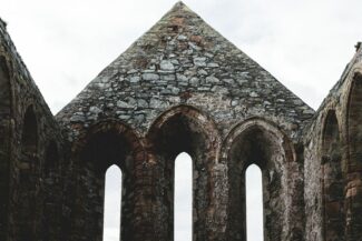 a stone building with three arched windows and a sky background